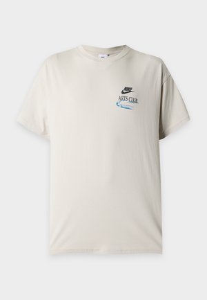 Μπεζ κοντομάνικη μπλούζα Nike με στρογγυλή λαιμόκοψη, μικρό μαύρο λογότυπο Nike και μπλε κείμενο "Arts Club" στο αριστερό στήθος.