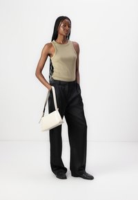 Beige ermeløs tanktop, svarte vide bukser og hvit håndveske. Glatt stoff med en tilpasset fasong og subtile detaljer. Ren bakgrunn.