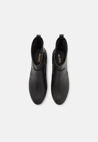 Bottines en cuir noir avec une surface lisse, bout arrondi, côtés élastiques et fermeture éclair. L'intérieur comporte un logo en relief.