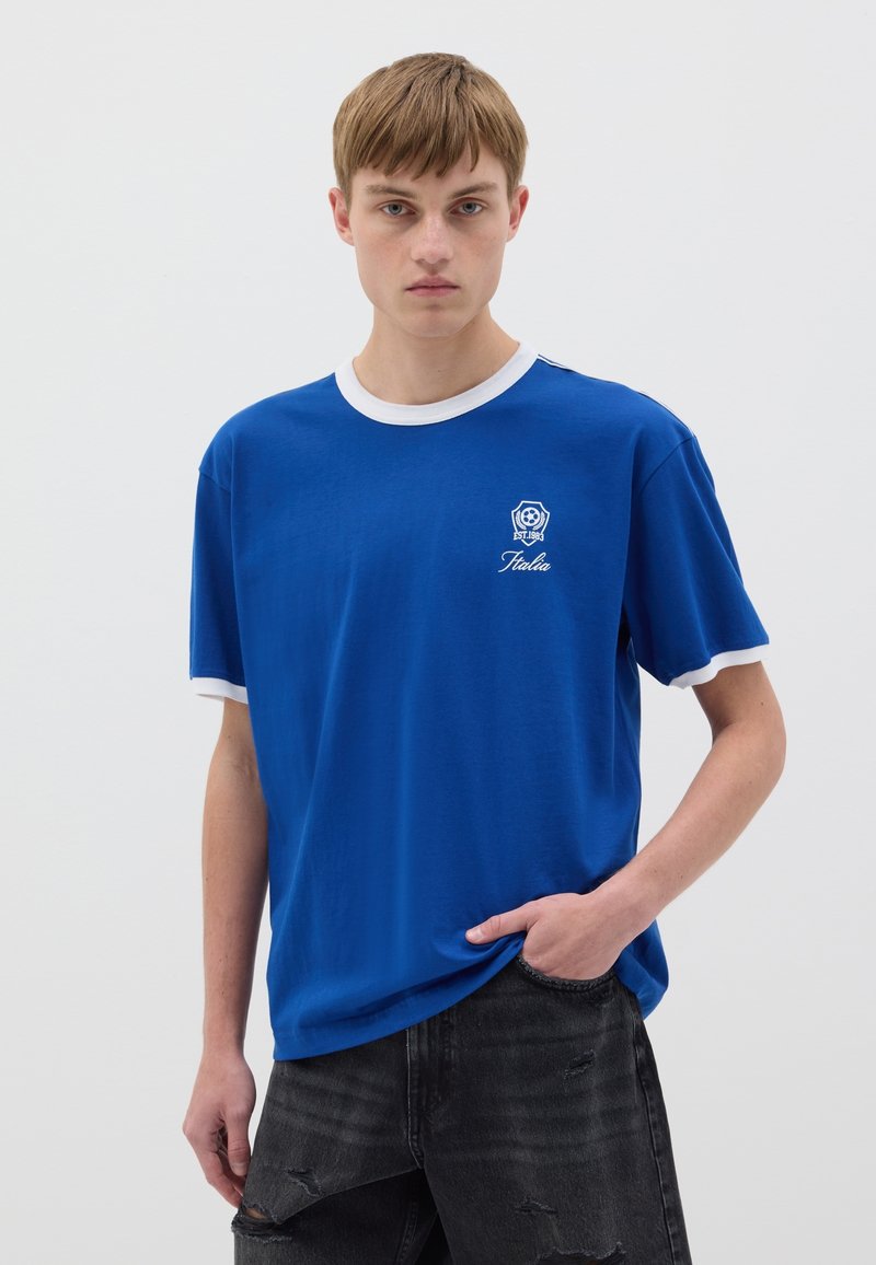 Blaues Baumwoll-T-Shirt mit weißem geripptem Kragen und Ärmelabschlüssen, mit einem kleinen Wappen-Logo und dem auf die Brust gestickten Text "Italia".