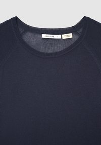 Marineblaues Strickoberteil mit Rundhalsausschnitt und strukturierter Oberfläche, mit einem Etikett mit der Aufschrift "CALLIOPE" und "ZERO WASTE DESIGN".