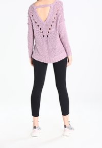 Světle fialový pletený svetr s výřezem na zádech a diamantovým vzorem. V kombinaci s černými legínami a šedými teniskami s bílou podrážkou.