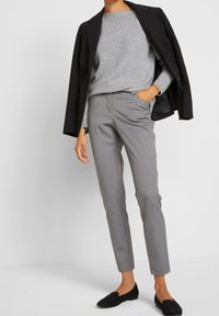 Grau strukturierter Strickpullover kombiniert mit maßgeschneiderten grauen Hosen und schwarzen Loafers. Ein Blazer liegt über den Schultern und betont das Outfit.