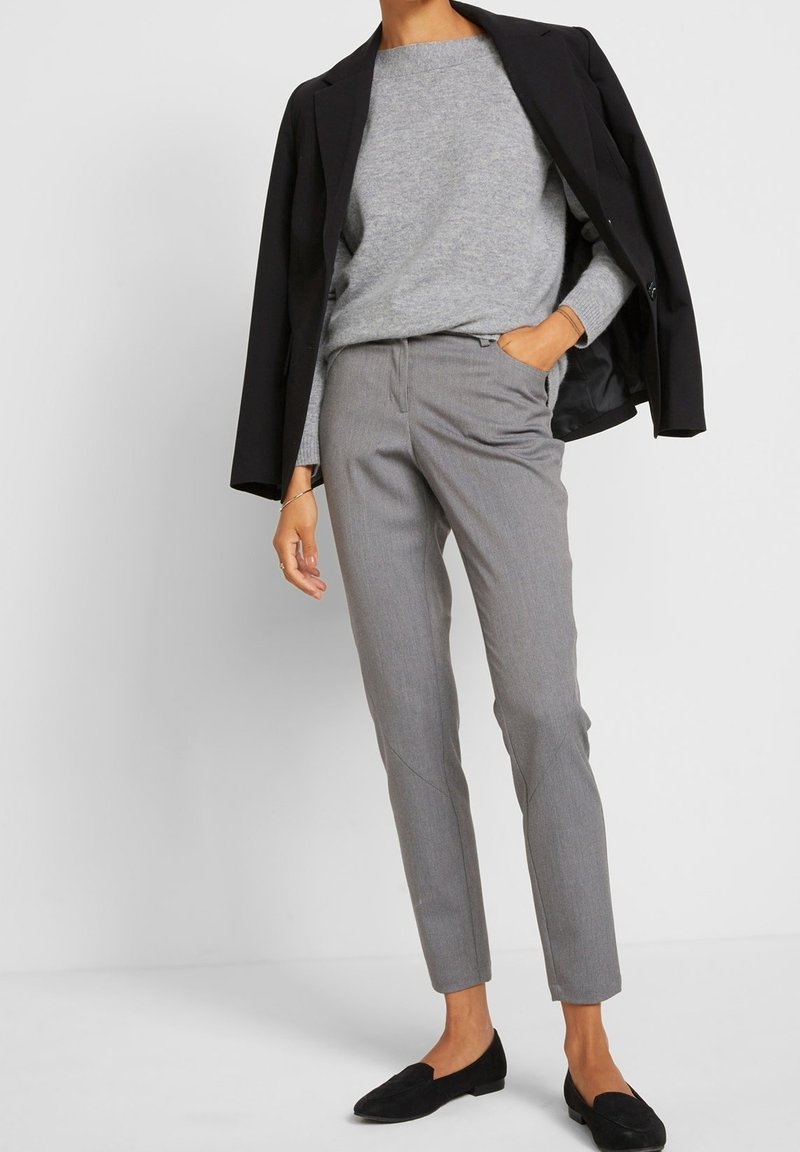 Grau strukturierter Strickpullover kombiniert mit maßgeschneiderten grauen Hosen und schwarzen Loafers. Ein Blazer liegt über den Schultern und betont das Outfit.