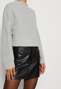 Osoba v světlém šedém pleteném svetru spárovaném s černou koženou mini sukni a průhlednými černými punčochami.