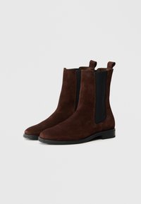 Barna velúr bokacsizma elasztikus oldalpanelekkel, lekerekített orral és lapos gumitalppal. Könnyű felhúzást biztosító kialakítás.