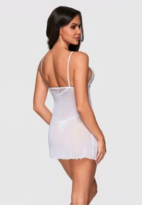 Lencería tipo babydoll con encaje blanco en los bordes, tirantes finos, tela transparente, un cuerpo ajustado y un dobladillo acampanado. Presenta bordes con forma de onda.