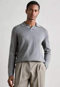 Hallis hallaste polo-sweater, millel on kaelus, sisaldab rinda peidetud logo ja on kombineeritud triibuliste, voldikatega pükstega.