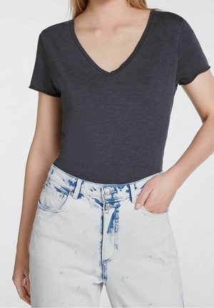 T-shirt noir, à manches courtes et en V, fabriqué en tissu léger et doux, associé à un jean taille haute déchiré bleu clair avec deux boutons.