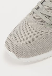 Chaussure de sport gris clair avec un empeigne en tricot texturé, lacets ton sur ton et une semelle en caoutchouc blanc avec un motif de semelle.