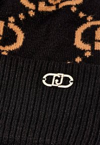 Black knitted fabric with a ribbed texture, featuring a tan pattern and a gold-toned decorative clasp integrated into the design.