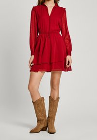 Abito rosso con scollatura alta, lunghe maniche trasparenti e gonna a strati. Abbinato a stivali da cowboy in suede color sabbia con dettagli ricamati.