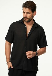 Schwarzes, kurzärmliges Hemd mit Knöpfen aus strukturiertem Material, mit einem Kragen und einer Brusttasche. Einfaches Design mit weichem, atmungsaktivem Stoff.