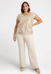 Top beige con lentejuelas, con escote en V y mangas cortas, combinado con pantalones de pierna ancha color crema y zapatos de punta neutra. Diseño texturizado y elegante.