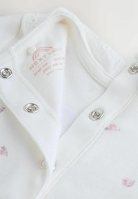 Fehér pamut baba body virágos mintával, ezüst kapcsokkal és a belső nyakrészen márkajelzéssel ellátott címkével.