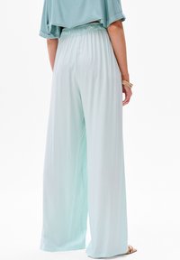 Lichte mintgroene wijde broek met een relaxte pasvorm, elastische tailleband en een soepele textuur. De stof valt zacht en reikt tot de vloeiende zoom.