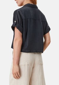 Blusa blu navy a maniche corte con colletto, dettaglio con piega sul retro e maniche arrotolate, abbinata a pantaloni di lino chiari.