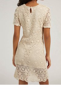 Robe en crochet crème avec des motifs hexagonaux et floraux, à manches courtes et une ouverture en clé à l'arrière. Détail de l'ourlet en forme de vagues au bas.