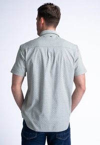 Camisa de botones de manga corta en tejido verde claro con un patrón geométrico, que cuenta con un cuello y una abertura en la parte posterior.