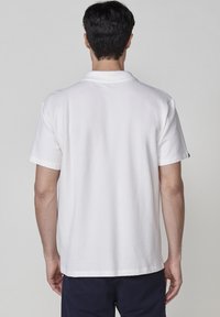 Vit kortärmad pikétröja av strukturerad våffelstickad tyg. Har en klassisk krage och en rak nederkant. Inga synliga varumärken.