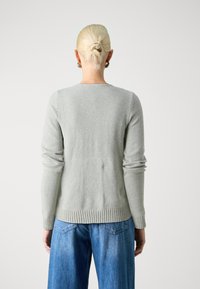 Maglione grigio chiaro in morbido materiale, con maniche lunghe, scollo rotondo e orli a costine, abbinato a jeans blu larghi.