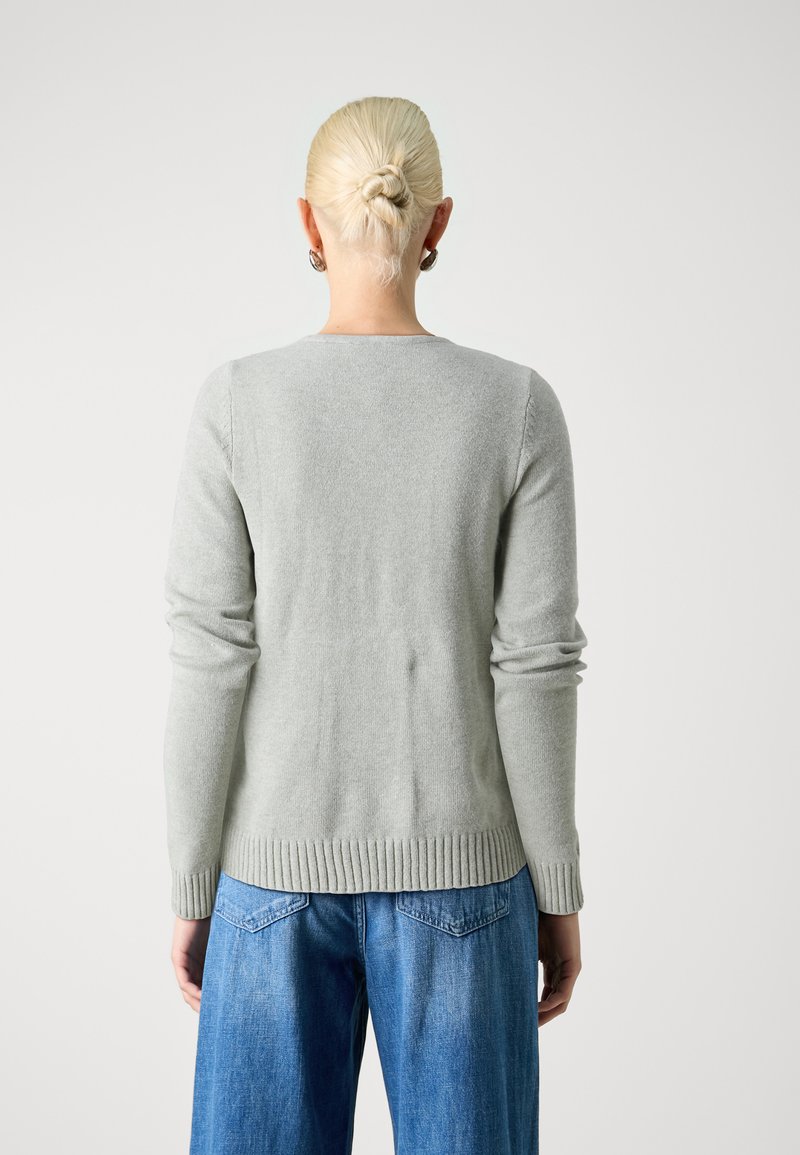 Un pull léger gris fabriqué dans un matériau doux, avec des manches longues, un col rond et des ourlets côtelés, porté avec un jean bleu ample.