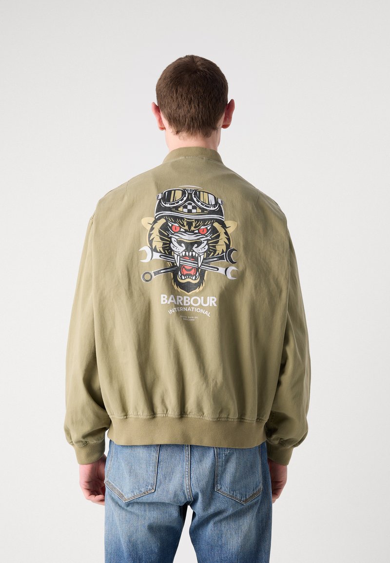 Khakifarbene Bomberjacke mit gerippten Bündchen und Saum, die auf dem Rücken eine große Grafik eines Tigers mit Schutzbrille und Schraubenschlüsseln zeigt.