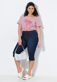 Camiseta corta a rayas rojas y blancas con un nudo en el frente, combinada con jeans capri de color azul oscuro. Los accesorios incluyen un bolso plateado y sandalias blancas.