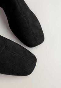 Schwarze Wildlederstiefel mit einem spitzen Ze design, die dezente Nähte und eine glatte Textur aufweisen. Keine sichtbaren Beschläge oder Akzente.