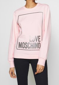 Pink long-sleeve sweatshirt with a black outlined rectangular design and "LOVE MOSCHINO" in bold metallic letters on the front. Cotton material.
