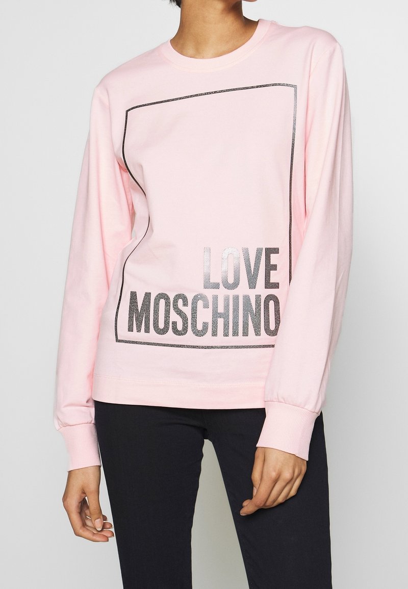 Růžová mikina s dlouhým rukávem s černě orámovaným obdélníkovým designem a nápisem "LOVE MOSCHINO" v tučných metalických písmenkách na přední straně. Bavlněný materiál.