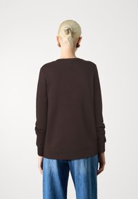 Sudadera marrón de manga larga, con cuello redondo y puños acanalados, combinada con jeans de pierna ancha de un azul claro. Textura suave y diseño casual.