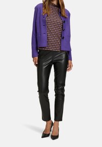 Chaqueta de mezcla de lana morada con botones negros, blusa estampada en marrón y naranja, y pantalones de cuero negros ajustados, complementados con tacones negros.