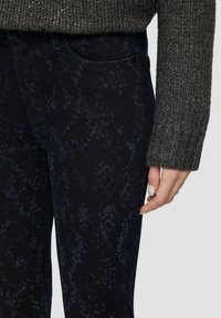 Ciemnoniebieskie dżinsy o subtelnym wzorze teksturowym, mające dopasowany krój i przednią kieszeń, połączone z szarym swetrem z dzianiny.