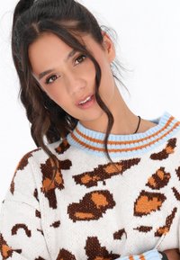 Maglione lavorato a maglia con una base bianca, caratterizzato da motivi irregolari arancioni e marroni. Collo a costine blu con strisce arancioni. Morbido al tatto.