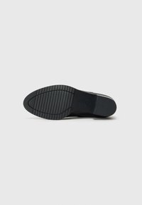 Black rubber sole with a textured pattern and logo. Features a rounded shape and flexible construction for comfort and traction.