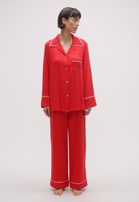 Κόκκινο σετ πυτζάμας με μακριά μανίκια και παντελόνια, με λευκές ραφές και τσέπη στο στήθος με μικρή κεντημένη λεπτομέρεια. Ομαλή υφή.