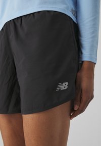 Black athletic shorts with a lightweight, smooth texture, featuring a reflective New Balance logo on the lower left side.
