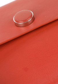 Gros plan d'une surface en cuir rouge avec un fermoir à bouton argenté sécurisant un rabat.