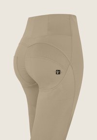 Leggings beige a vita alta, dalla vestibilità aderente, con una texture liscia, cuciture curve e un piccolo logo nero sul lato.