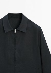 Veste noire à manches longues avec col et fermeture éclair devant sur fond blanc.