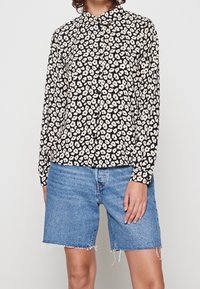 Blusa nera con motivo floreale bianco, colletto, maniche lunghe; abbinata a pantaloncini di jeans blu, orlo sfrangiato, fit rilassato.