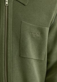 Kurtka zapinana na zamek w kolorze oliwkowej zieleni, wykonana z miękkiego materiału. Posiada kołnierz oraz kieszeń na piersi z haftowanym logo marki.