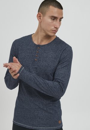Tumesinine pika varrukaga henley-särk, millel on tekstuuriline muster, viis pruuni nööpi ja kontrastne äär.