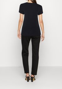 Sort kortærmet t-shirt med lige kant og rund halsudskæring, parret med højtaljede sorte jeans og sorte hælede sandaler.