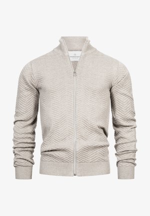 Licht beige gebreide trui met rits en chevronpatroon, geribbelde boorden, kraag en zoom, weergegeven op een witte achtergrond.