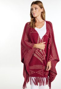 Burgundy poncho yang menampilkan pola geometris emas dan detail poni di bagian hem, terbuat dari material yang lembut dan berbahan tekstur.