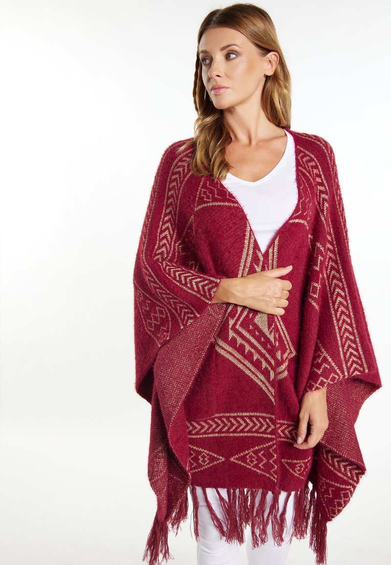 Burgundy poncho yang menampilkan pola geometris emas dan detail poni di bagian hem, terbuat dari material yang lembut dan berbahan tekstur.