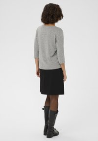 Siva majica s tričetvrtastim rukavima od teksture pletenine, u kombinaciji s crnom suknjom. Crne čizme do koljena s dekorativnom trakom i kopčom.