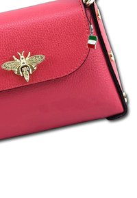 Sac à main en cuir rose avec un emblème d'abeille en or, des accents noirs et des clous décoratifs. Le charme attaché présente un petit design du drapeau italien.